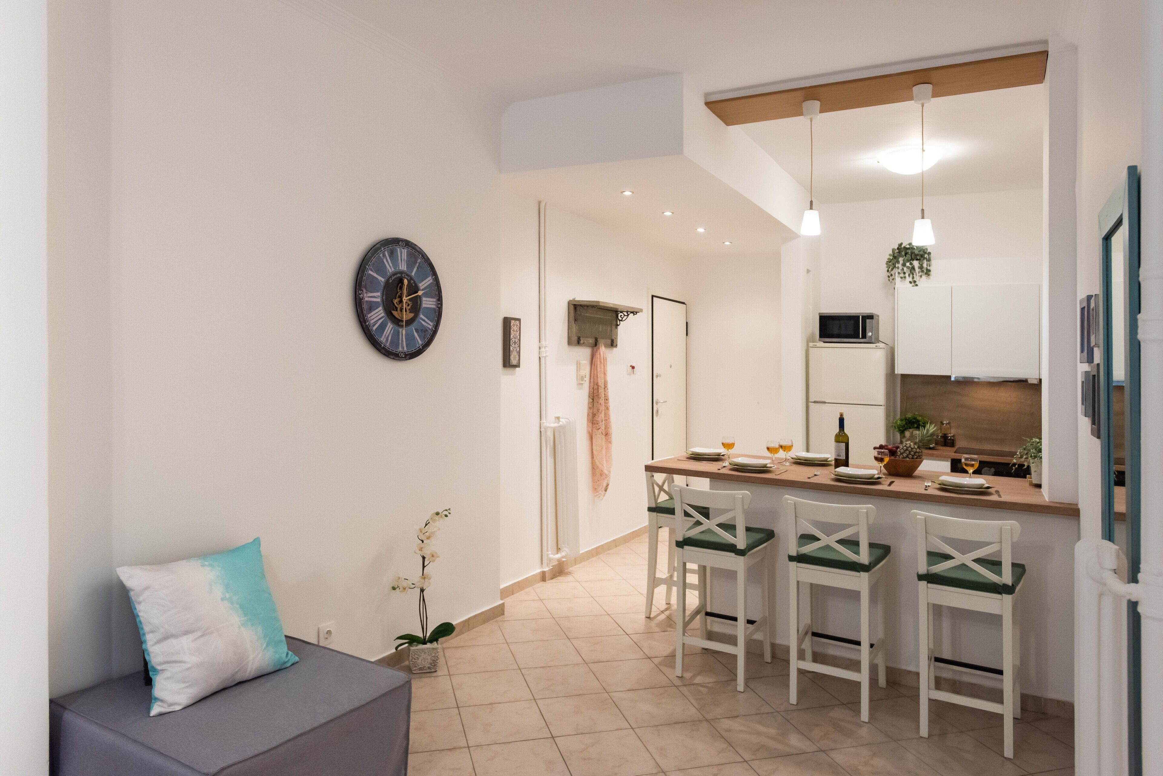 A modern kitchen with a bar area, white cabinets, and a clock on the wall.