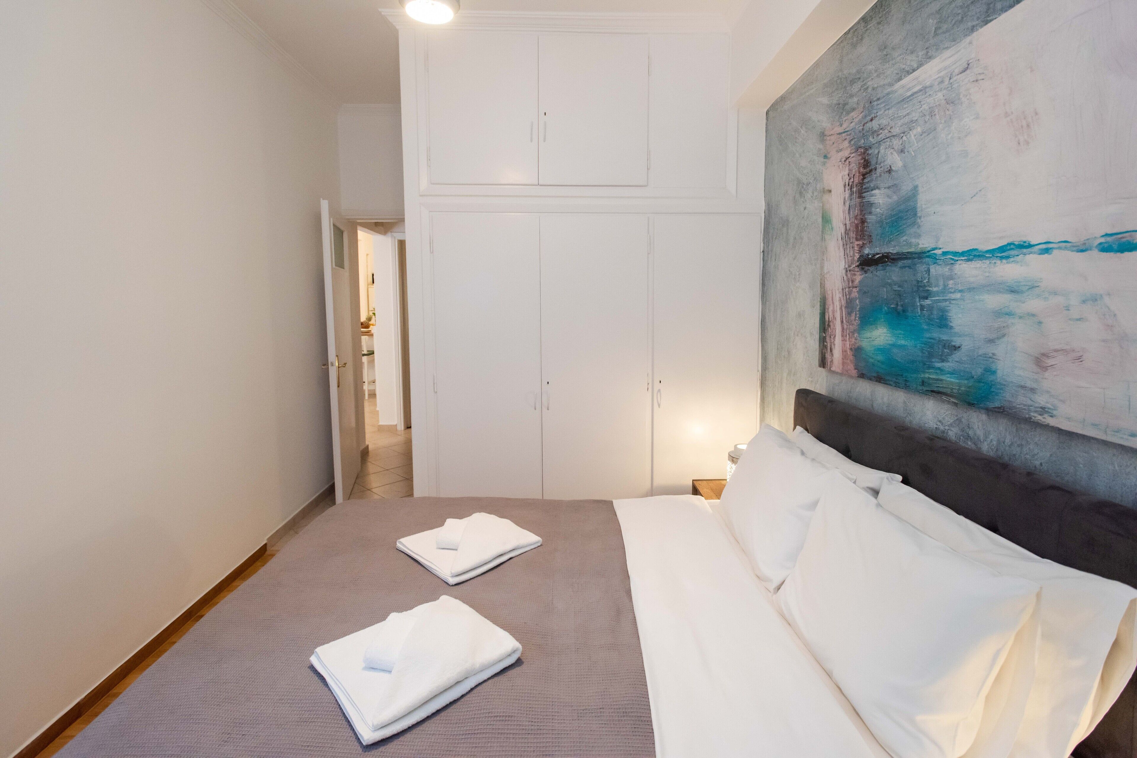 A hotel room with a bed, a large abstract painting, and a wardrobe.