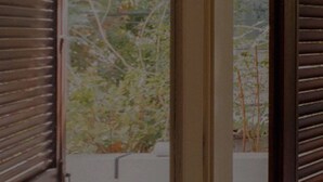 A window with wooden shutters partially open, revealing a view of greenery outside. - Modern and Central 2BD Apartment in TLV (Tel Aviv)