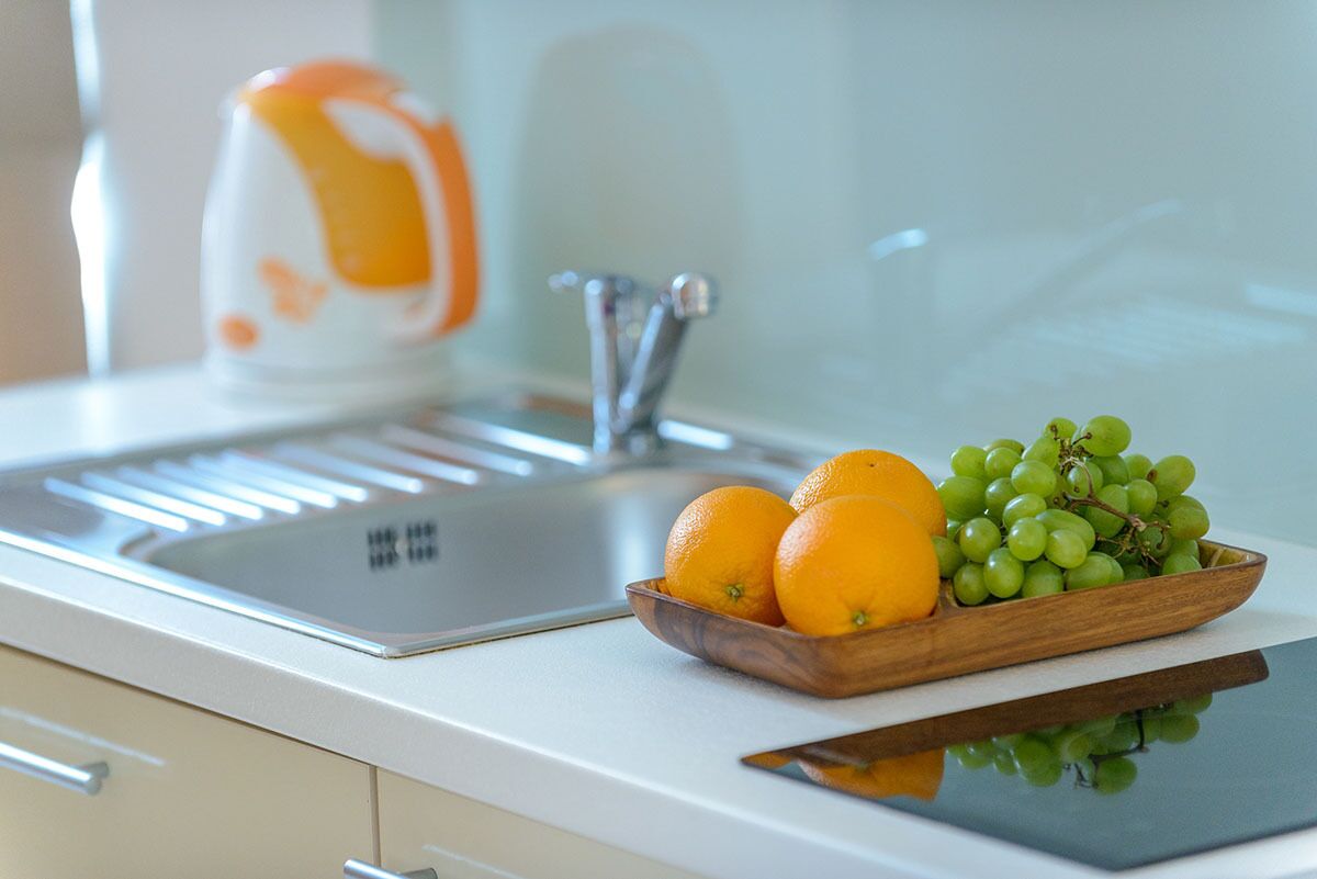 Een aanrecht met een spoelbak, een waterkoker en een houten kom met sinaasappels en druiven.