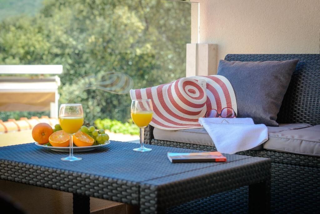 Un sofá de mimbre con un cojín, una mesa con un vaso de jugo de naranja, un plato con fruta y un vaso de jugo de naranja.