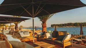 A deck with wooden furniture and umbrellas overlooking a beach. - Adriatic Resort Apartments (Dubrovnik)
