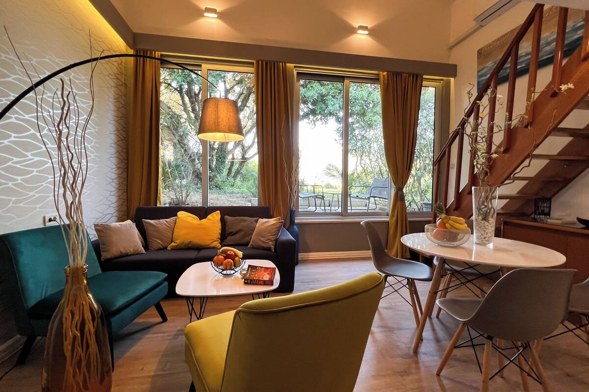 Ein modernes Wohnzimmer mit einer Couch, einem Couchtisch und Sesseln, einem Esstisch mit einer Vase und einer Treppe.