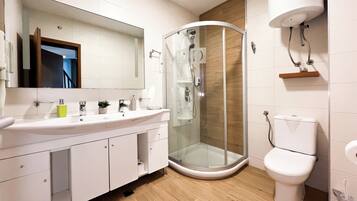 A modern bathroom with a glass-enclosed shower, a white toilet, and a large mirror above the sink.