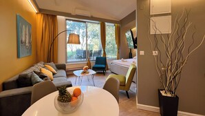 A modern living room with a sofa, a dining table with fruit, a lamp, and a view of the outdoors. - Adriatic Resort Apartments (Dubrovnik)