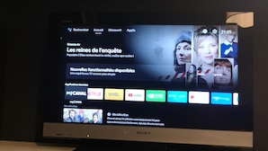 Et fjernsyn der viser en streamingtjenestes brugerflade med forskellige app-ikoner og et billede hængt over.