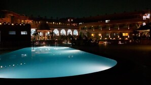 Vista nocturna de una piscina con el reflejo de un edificio de ventanas arqueadas y una cúpula.