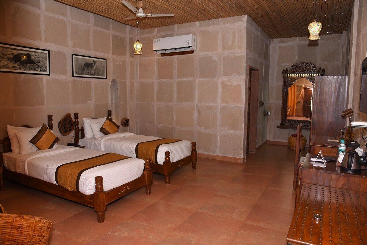 Una habitación con dos camas de madera, un ventilador de techo, un equipo de aire acondicionado y una zona de comedor con mesa y sillas.