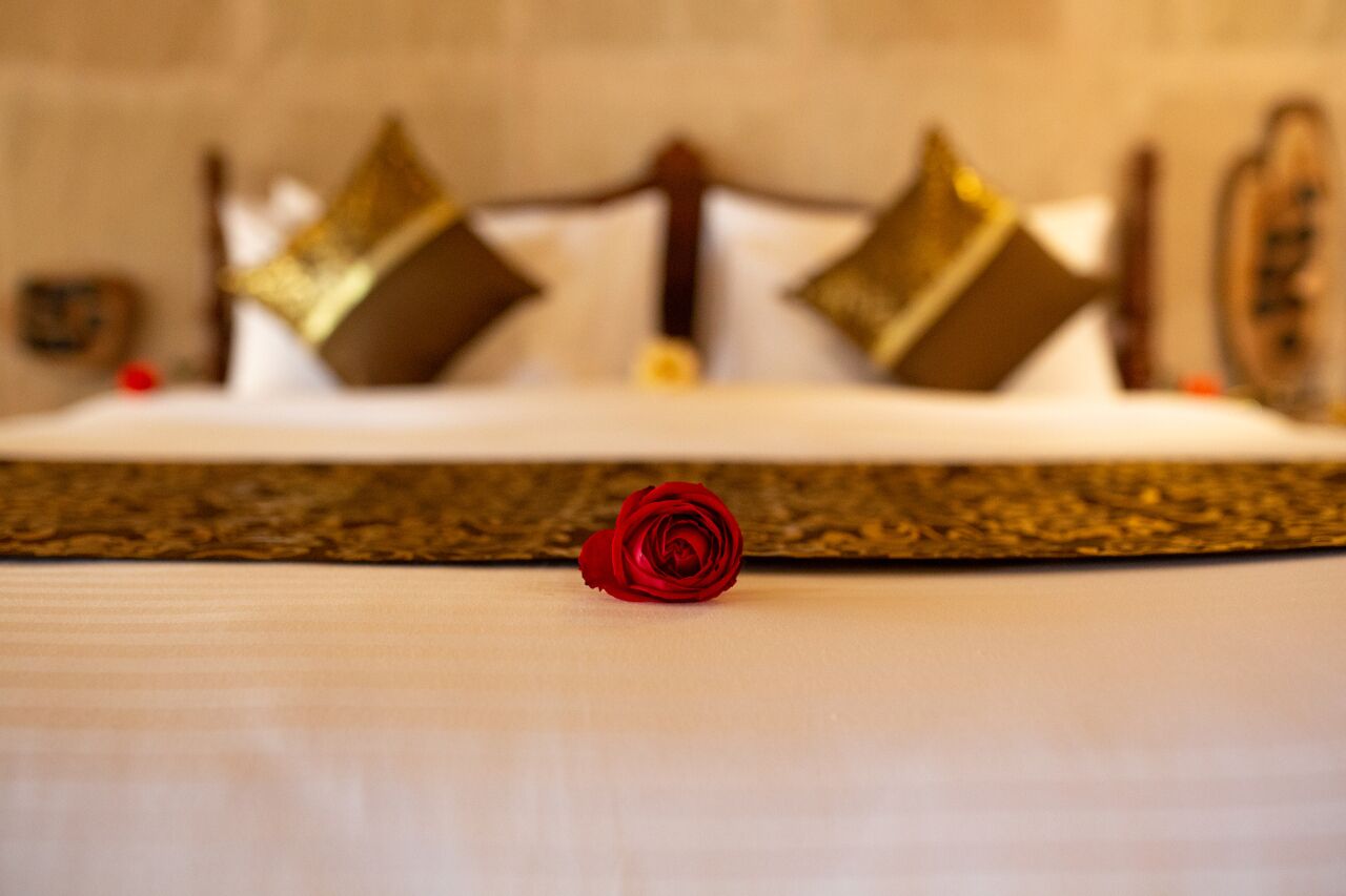 A bed with a white sheet and a single red rose in the center.