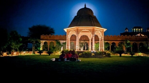 Un edificio grande e iluminado con una cúpula y estructuras en arco, rodeado de una zona de jardín bien iluminada.