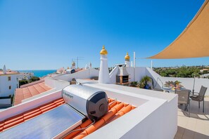 Een terras op het dak met een zonneboiler, een tafel met stoelen en uitzicht op zee en gebouwen.