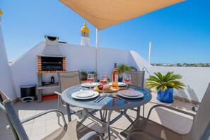 Een terras met een barbecue, stoelen en een tafel voor twee, compleet met wijnglazen en een fles wijn.