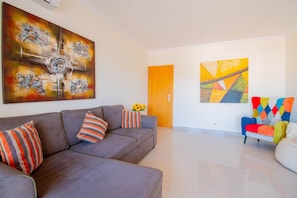 Una sala de estar moderna con un sofá gris, cojines coloridos y pinturas abstractas en las paredes.