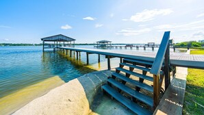 Un muelle que se adentra en una superficie acuática tranquila, con una zona de estar cubierta y una plataforma de hormigón.
