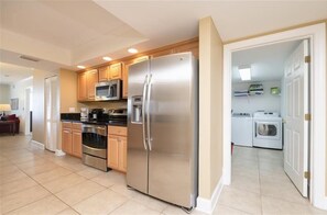 A modern kitchen with stainless steel appliances, wooden cabinets, and a laundry area.