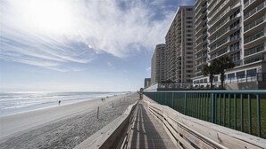 Une promenade en bois longeant une plage, avec des immeubles de grande hauteur en arrière-plan.