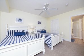Ein Schlafzimmer mit zwei Betten, einem Deckenventilator und einer Tür zu einem Badezimmer.