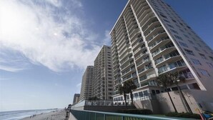 Un hôtel de grande hauteur doté de nombreux balcons, offrant une vue sur la plage et s’ouvrant sur un ciel dégagé.