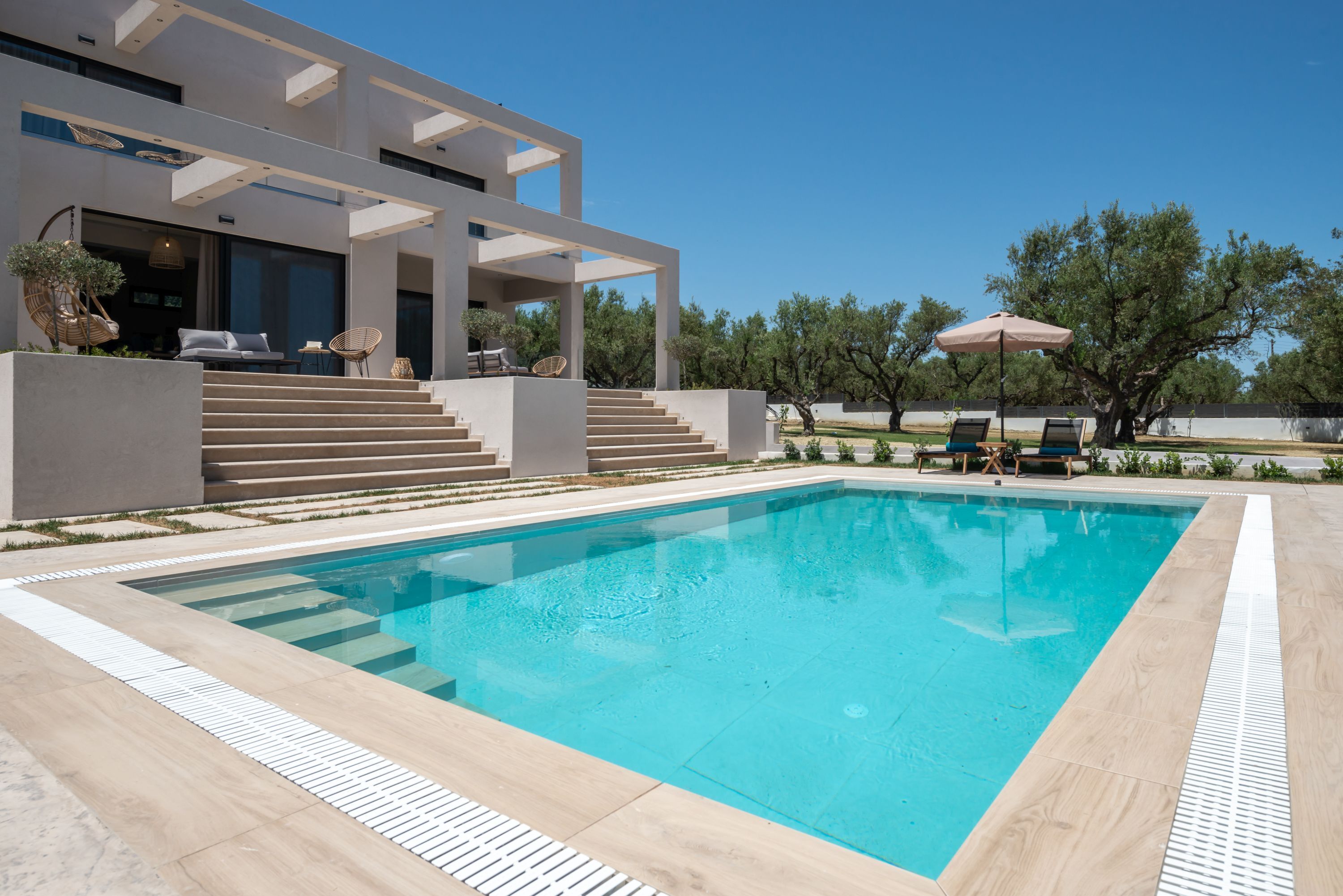 A modern house with a swimming pool, outdoor seating, and a staircase leading to the entrance.