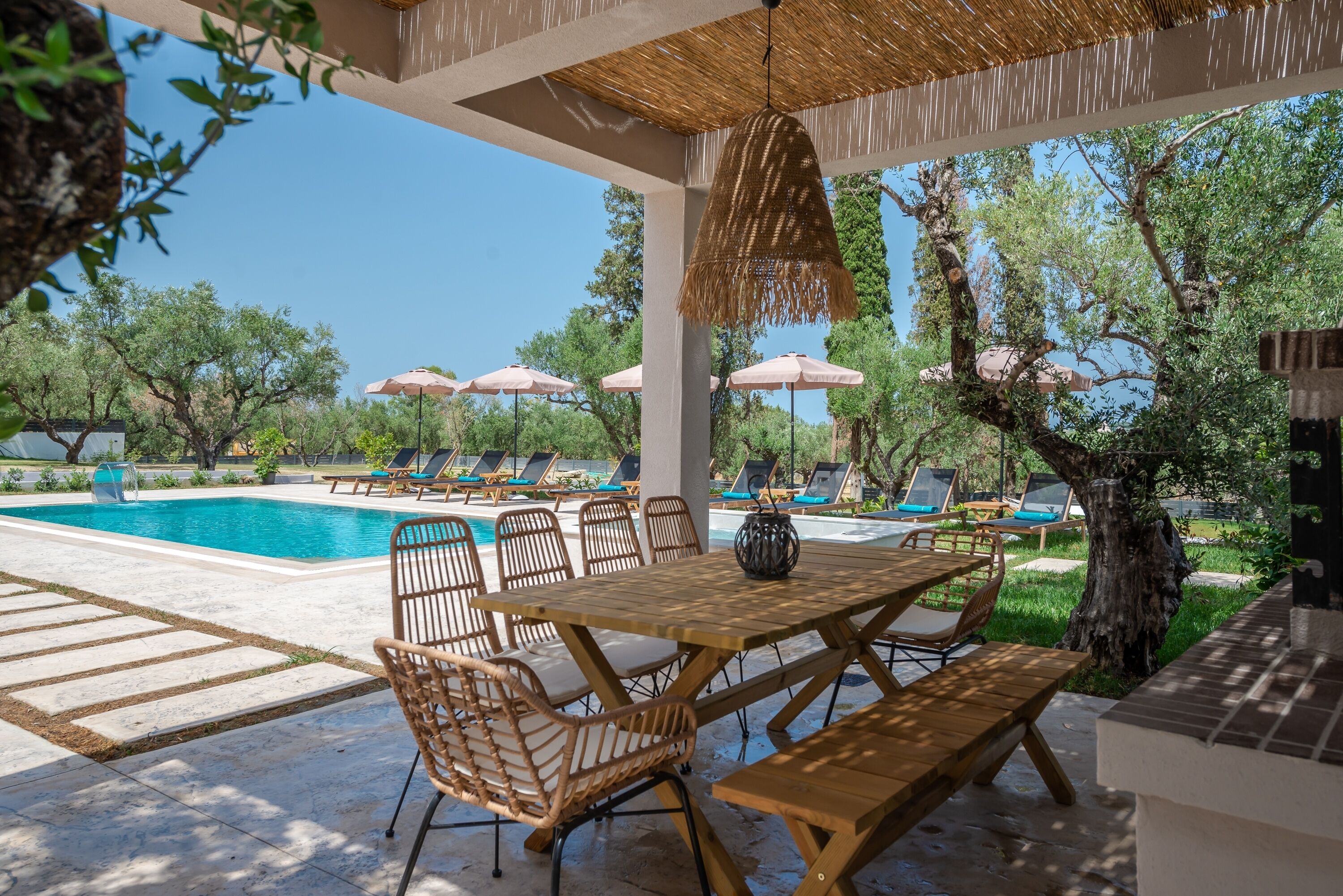 A poolside area with lounge chairs, umbrellas, and a wooden table and benches.