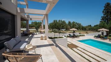 Relax by the pool in a serene outdoor space with a covered patio, seating, and a beautiful garden view.