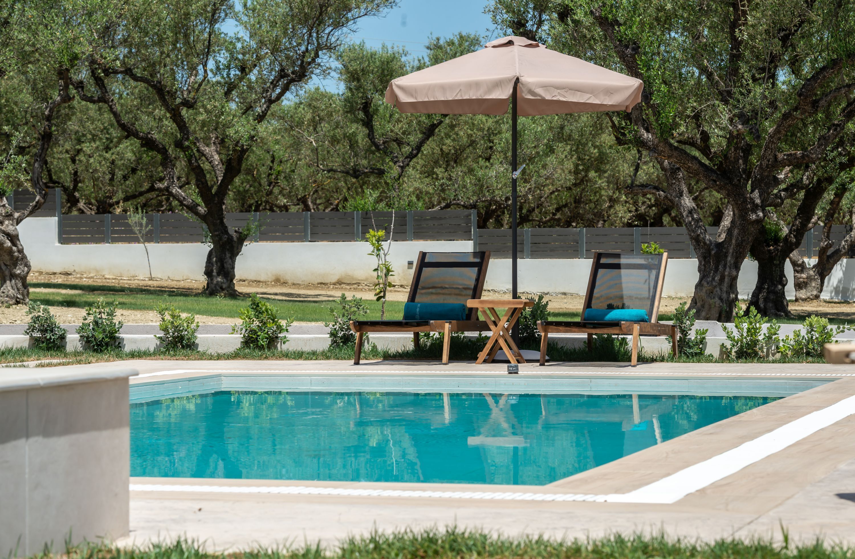 Piscina con dos sillas reclinables y una sombrilla grande.