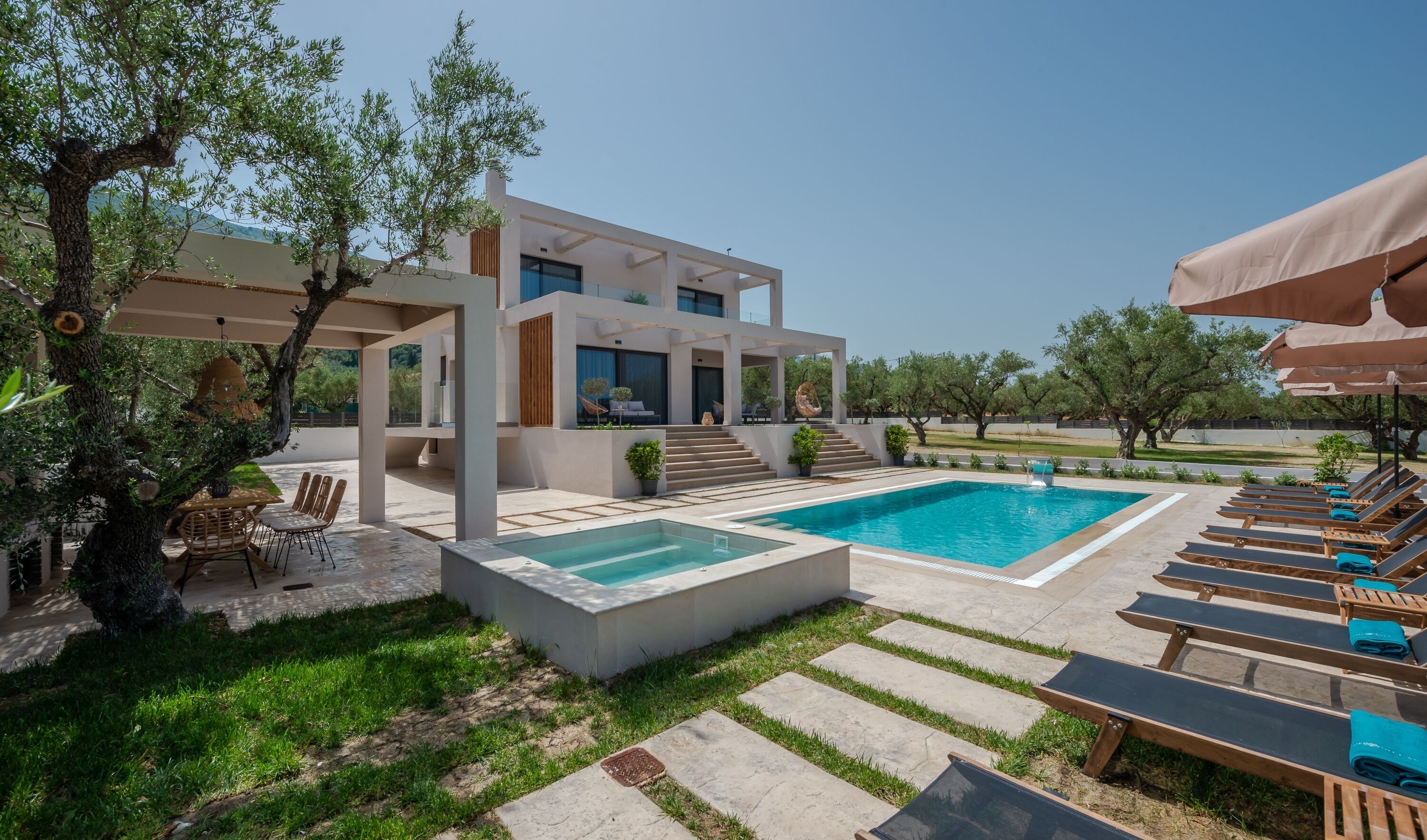 Una villa moderna con piscina, mobiliario exterior y jardín.