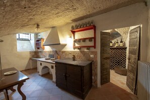 Une cuisine rustique avec un mur en pierre, des armoires en bois et une étagère rouge où sont posées des bouteilles.