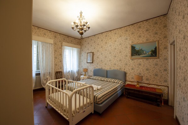 Un dormitorio con una cuna, una cama, una mesita de noche, una lámpara y un cuadro en la pared.