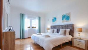 A bedroom with a bed, bedside tables, a nightstand, a window with curtains, and artwork on the wall. - Villa Alfazema | 5 Bedrooms | Quiet Area | Albufeira (Albufeira)