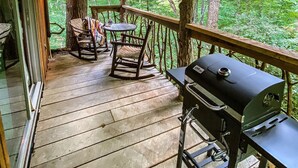 Eine Holzterrasse mit Grill und Sitzbereich mit Blick auf einen Wald.