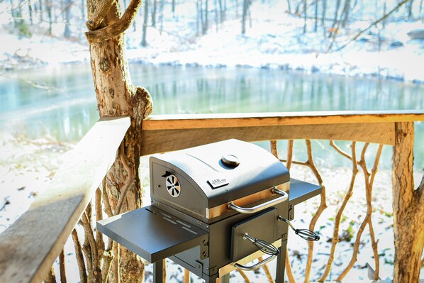 A portable grill with a digital display, positioned on a wooden deck overlooking a body of water.