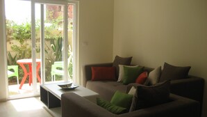 A living room with a sofa, a coffee table, and a small table with chairs. There is a sliding glass door leading to an outdoor area with a table and chairs. - Seaside (200m to beach), bright, spacious ground floor apartment, Les Dunes S+2 (Akouda)