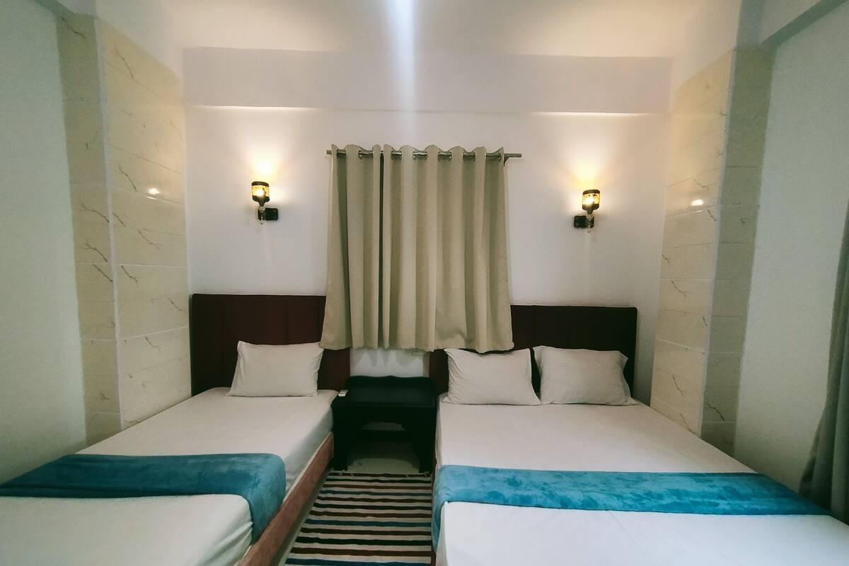 A hotel room with two single beds, a striped rug, and two wall-mounted lights.