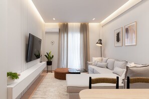 A modern living room with a flat-screen TV, a sofa, a coffee table, and a dining table. - Acropolis White Key Residence (Athens)