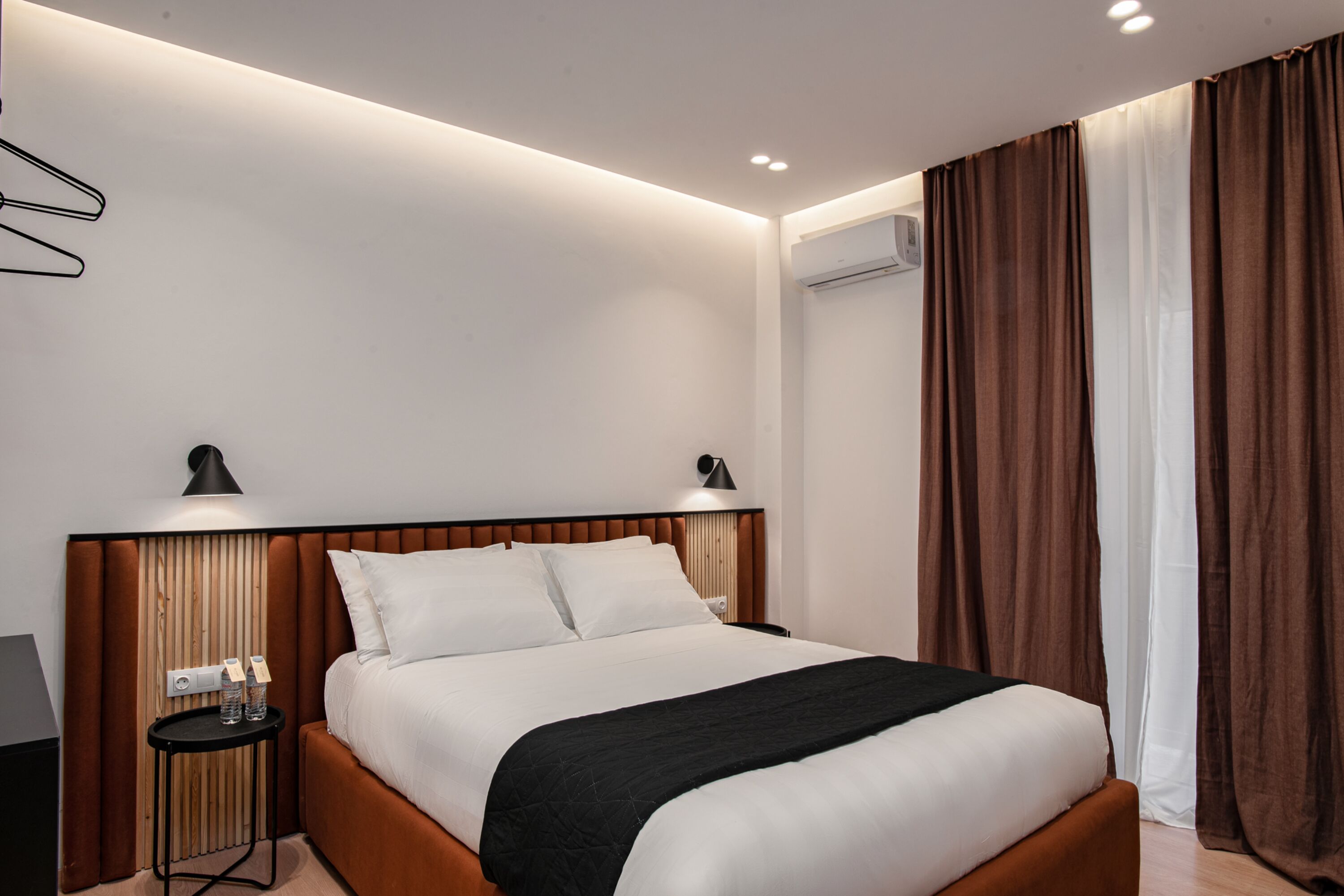 Una habitación de hotel moderna con una cama grande, una mesita de noche con lámpara y aire acondicionado instalado en la pared.