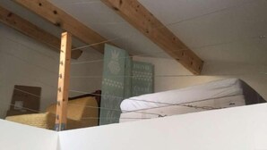 Quarto estilo loft com vigas de madeira aparente, beliche, armário de madeira e uma porta que dá para outro cômodo.