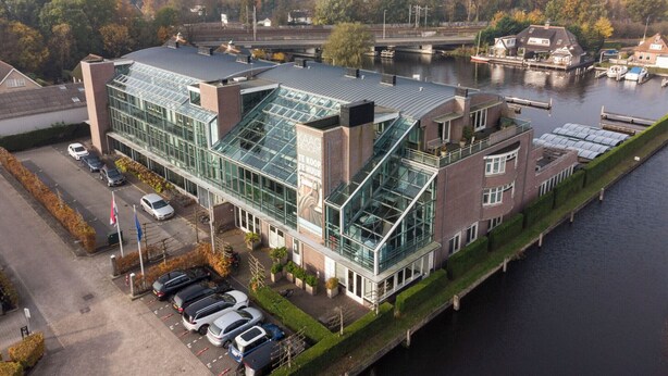 Een modern gebouw met een glazen gevel, een parkeerplaats en een rivier op de achtergrond.