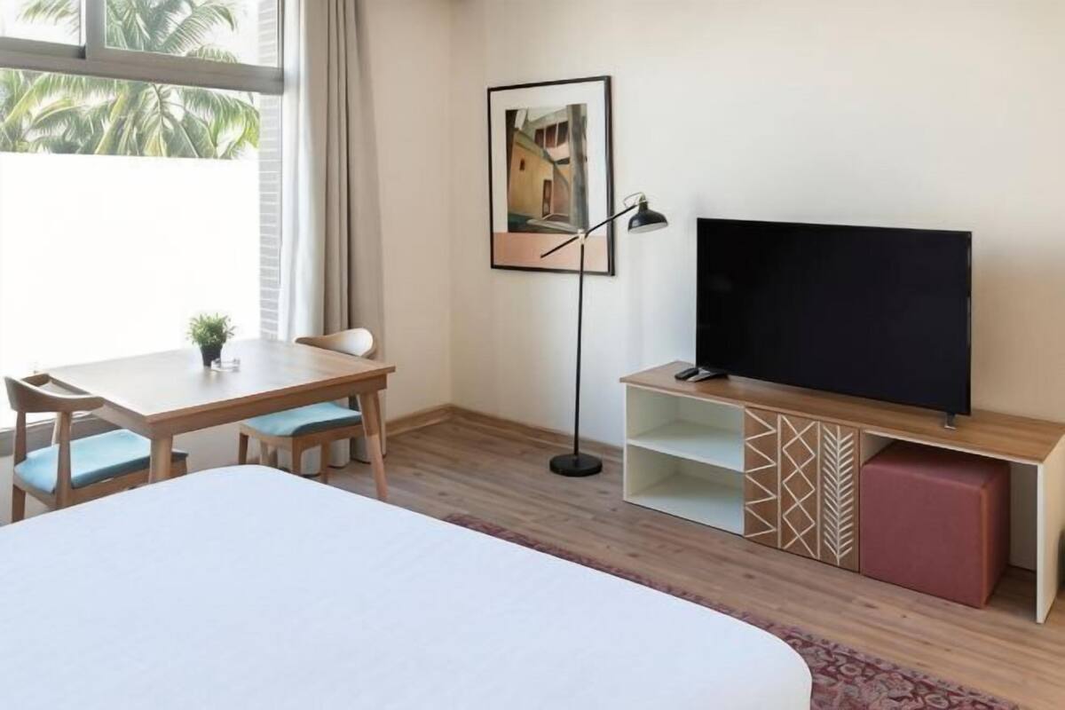 A hotel room with a bed, a desk with a chair, a television, and a framed picture on the wall.
