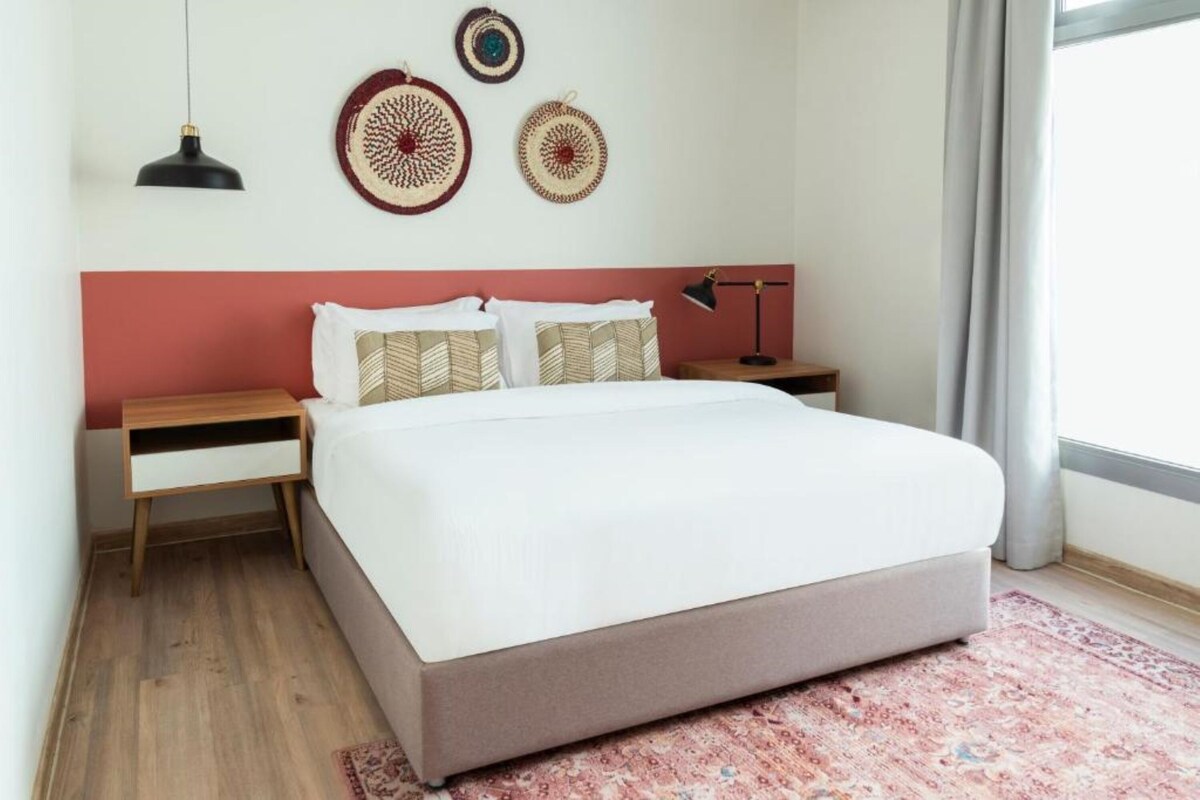 Un dormitorio con una cama, dos mesitas de noche, una lámpara y adornos en la pared.