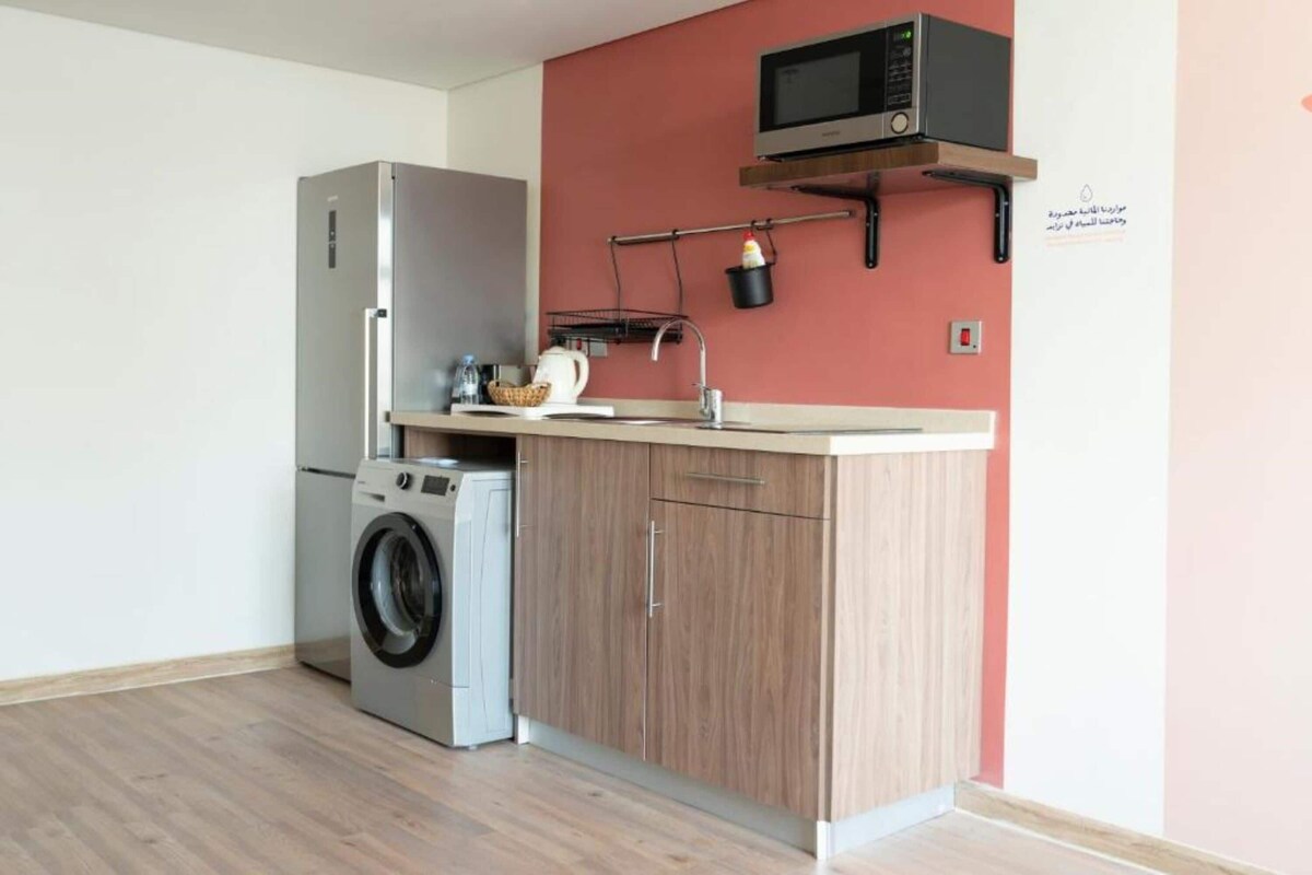 A compact kitchen with a washing machine, a microwave, and a wooden cabinet.