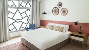 Una camera da letto moderna con un letto grande, una poltrona blu, un comodino in legno, una scrivania e una finestra con motivo geometrico.