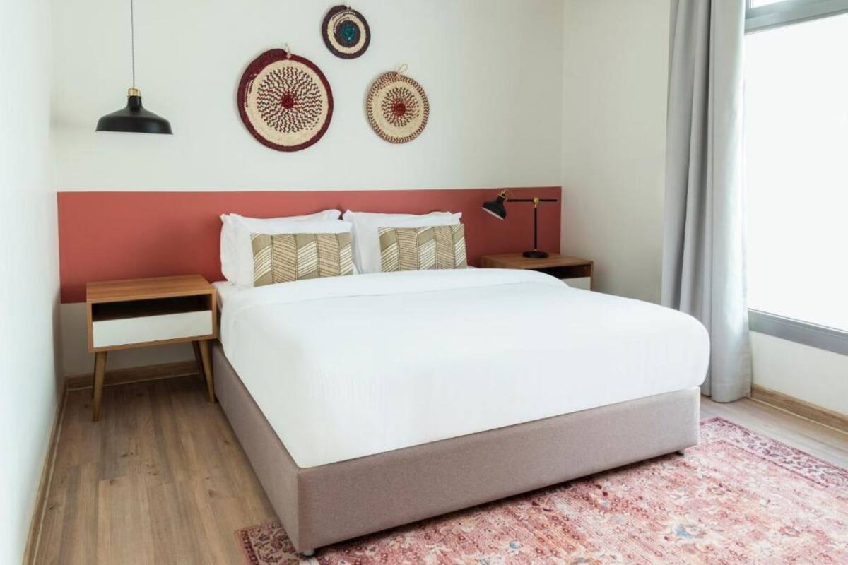 A bedroom with a bed, two bedside tables, a nightstand, a hanging lamp, and decorative wall hangings.