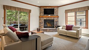 Ein Wohnzimmer mit Kamin aus Stein, zwei Sofas, einem Couchtisch und großen Fenstern.