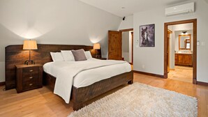 Ein Schlafzimmer mit einem hölzernen Bett, zwei Nachttischen mit Lampen, einem weißen Teppich und einem Flur, der zu einem Badezimmer mit Holzschränken führt.