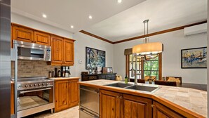 Eine moderne Küche mit Holzschränken, Edelstahlgeräten, einer großen Kochinsel mit Spüle und Bildern an den Wänden.