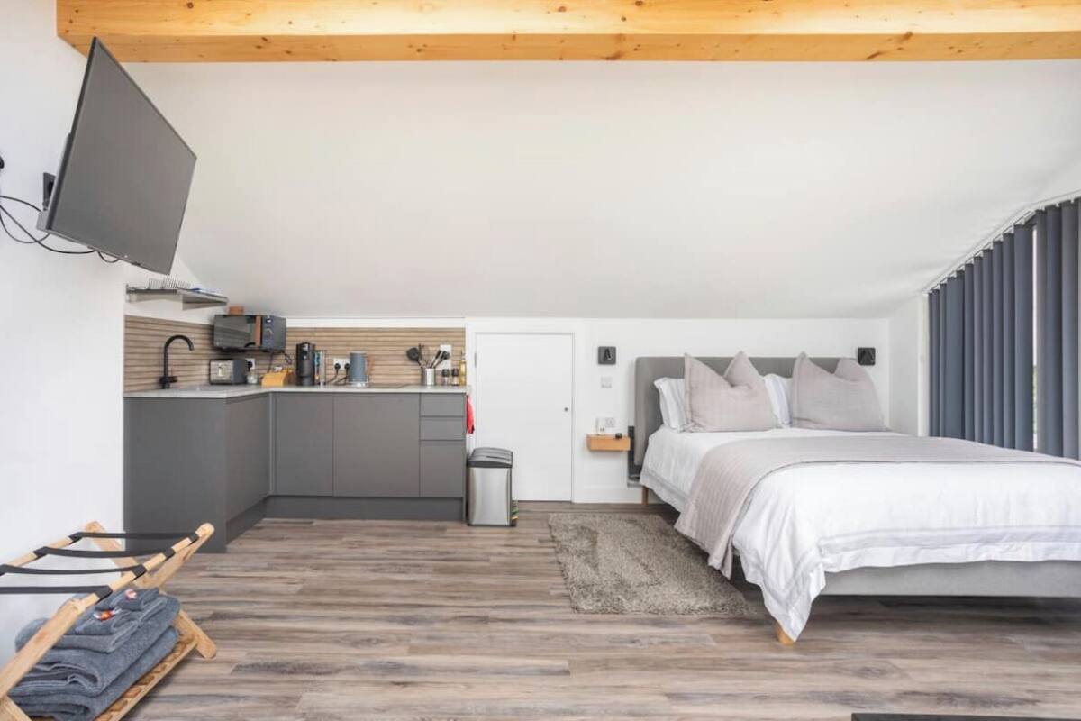 A compact bedroom with a bed, a small kitchenette, and a TV mounted on the wall.