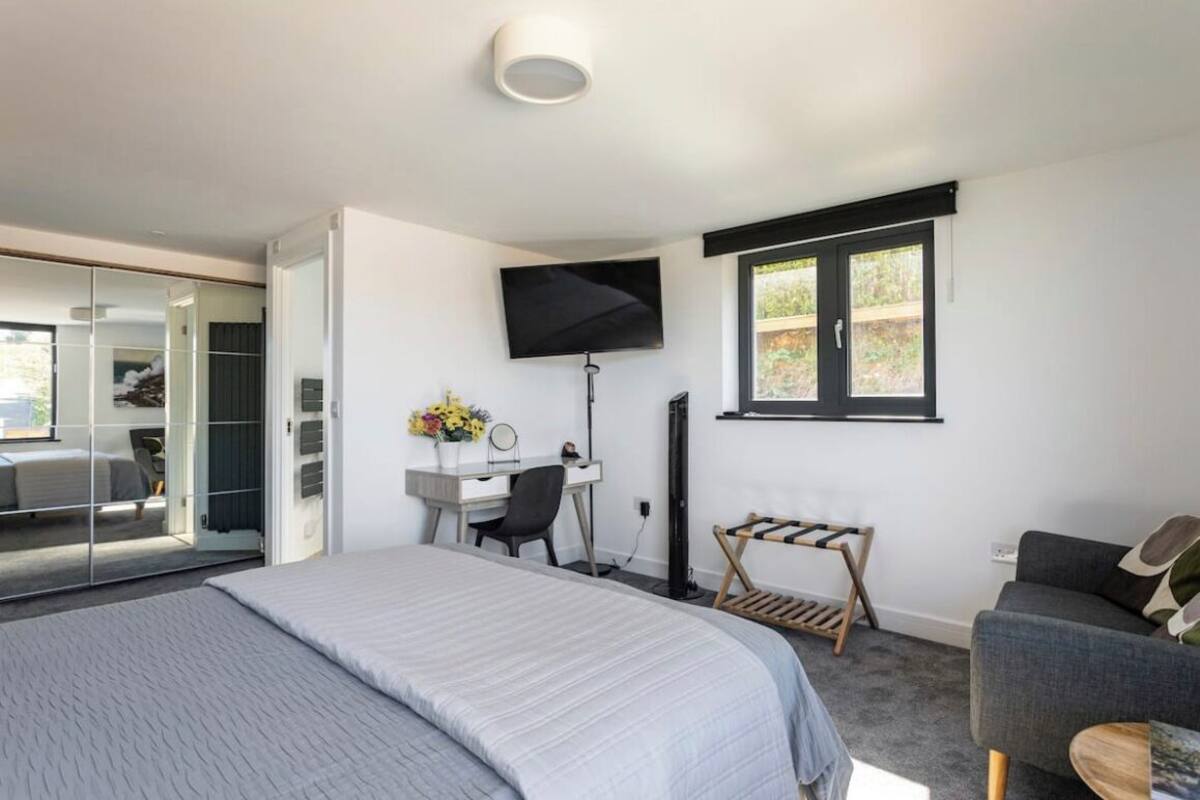 A modern bedroom with a bed, desk, chair, and a TV mounted on the wall.