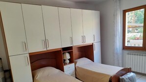Ett rum med två separata sängar, en garderob, ett litet bord och ett fönster med utsikt över grönområden.