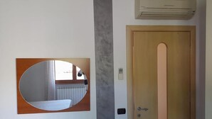 Ett rum med en dörr av trä, en väggmonterad luftkonditioneringsanläggning och en spegel som reflekterar ett fönster och ett element.